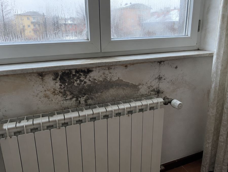 Parete sotto una finestra con macchie di muffa sopra il termosifone